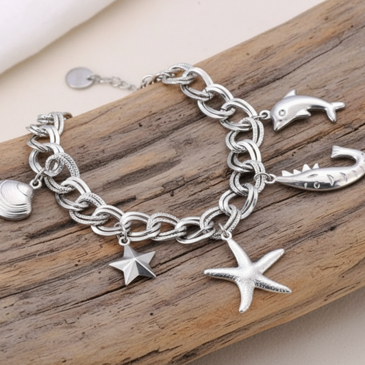 Pulseira uma corrente de elos duplos trabalhados e pendentes detalhados em aço inoxidável — concha, estrela-do-mar, golfinho e cauda de baleia — esta peça é a celebração perfeita da vida marinha.